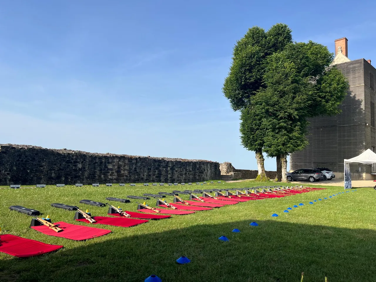 Pas de tir en plein air : carabines laser sur tapis rouges alignés sur la pelouse, au pied de remparts en pierre