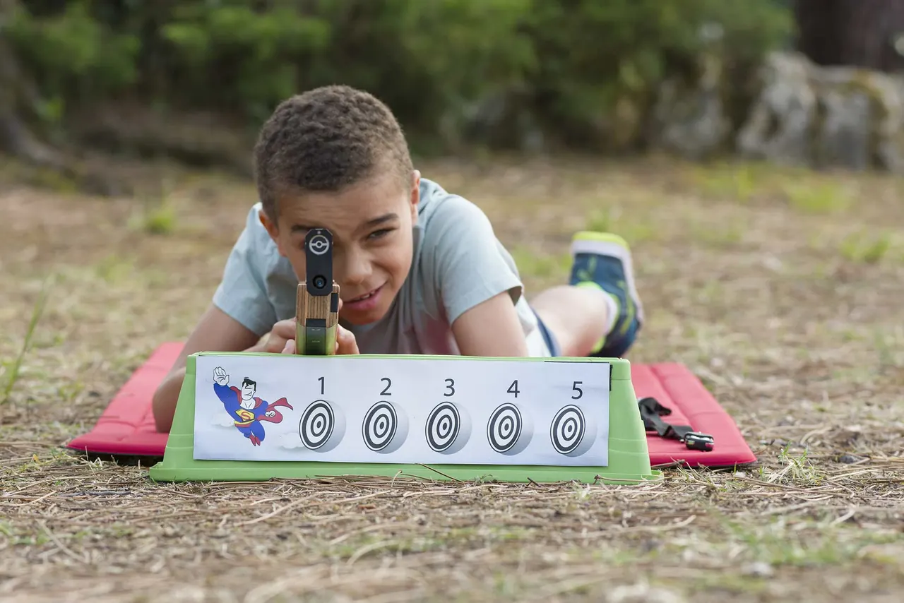 Jeune participant en position de tir couché sur un tapis rouge, devant une cible à cinq visuels